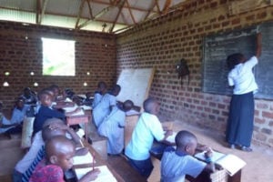 A teacher writing on a blackboard in front of students in a classroom in Uganda