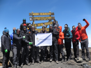 A group of people holding a sign atop Mount Kilimanjaro